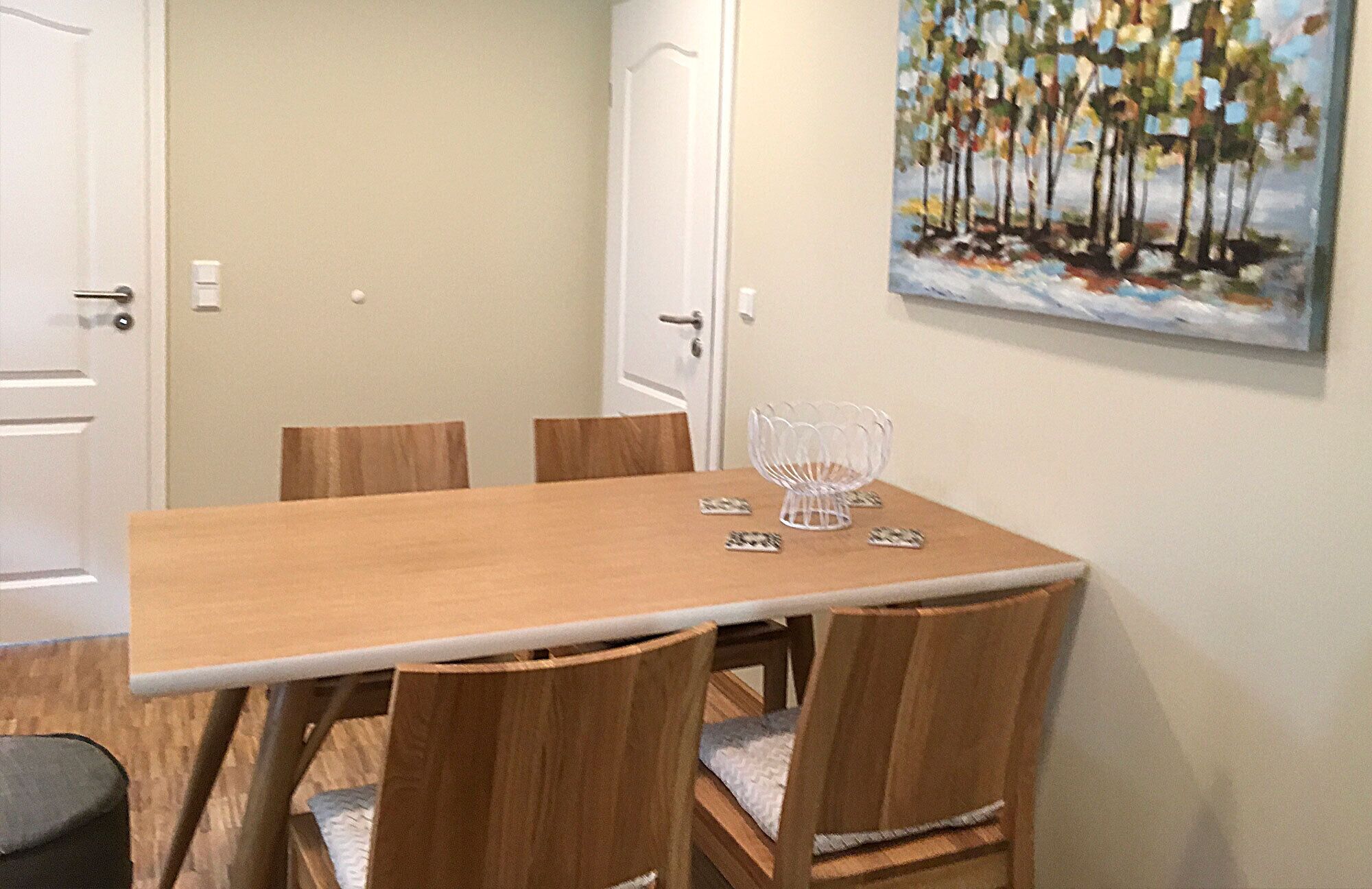 Un comedor con mesa y sillas de madera, un cuenco de vidrio decorativo y un cuadro en la pared.