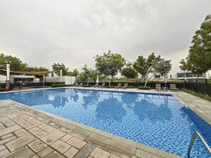 En rektangulær swimmingpool med flisekant, omgivet af en belagt terrasse.