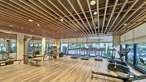 Ein Fitnessraum mit Trainingsgeräten, großen Fenstern und einer Holzbalkendecke.