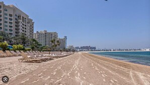A beach with sun loungers, a pier, and high-rise buildings in the background. - 1 Bed on The Palm l City Views l Near Atlantis (Palm Jumeirah)