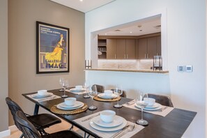 A dining area with a table set for six, a kitchen in the background, and a framed poster on the wall. - 1 Bed on The Palm l City Views l Near Atlantis (Palm Jumeirah)