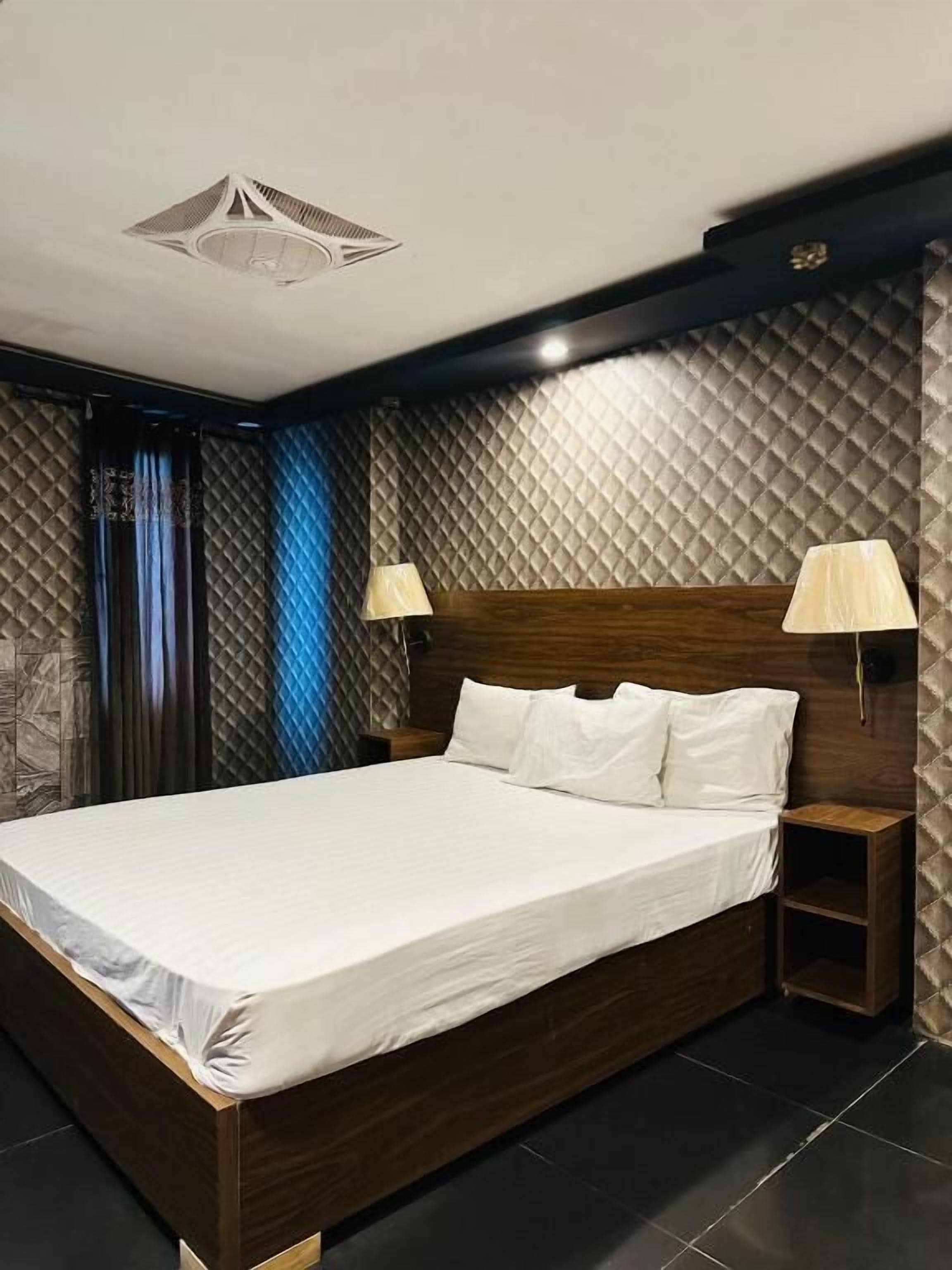 Habitación de hotel moderna con una cama grande, dos mesitas de noche y un diseño de techo original.