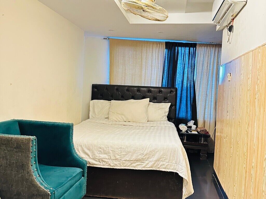 A hotel room with a bed, a chair, a nightstand, and a window with curtains.