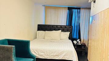 A hotel room with a bed, a chair, a nightstand, and a window with curtains.