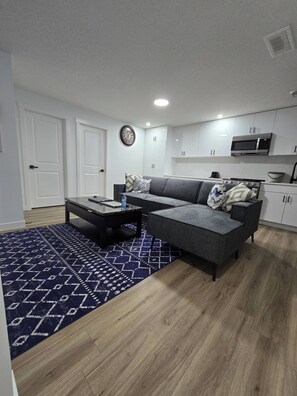 Ein modernes Wohnzimmer mit einem grauen Ecksofa, einem Couchtisch und einem gemusterten Teppich.