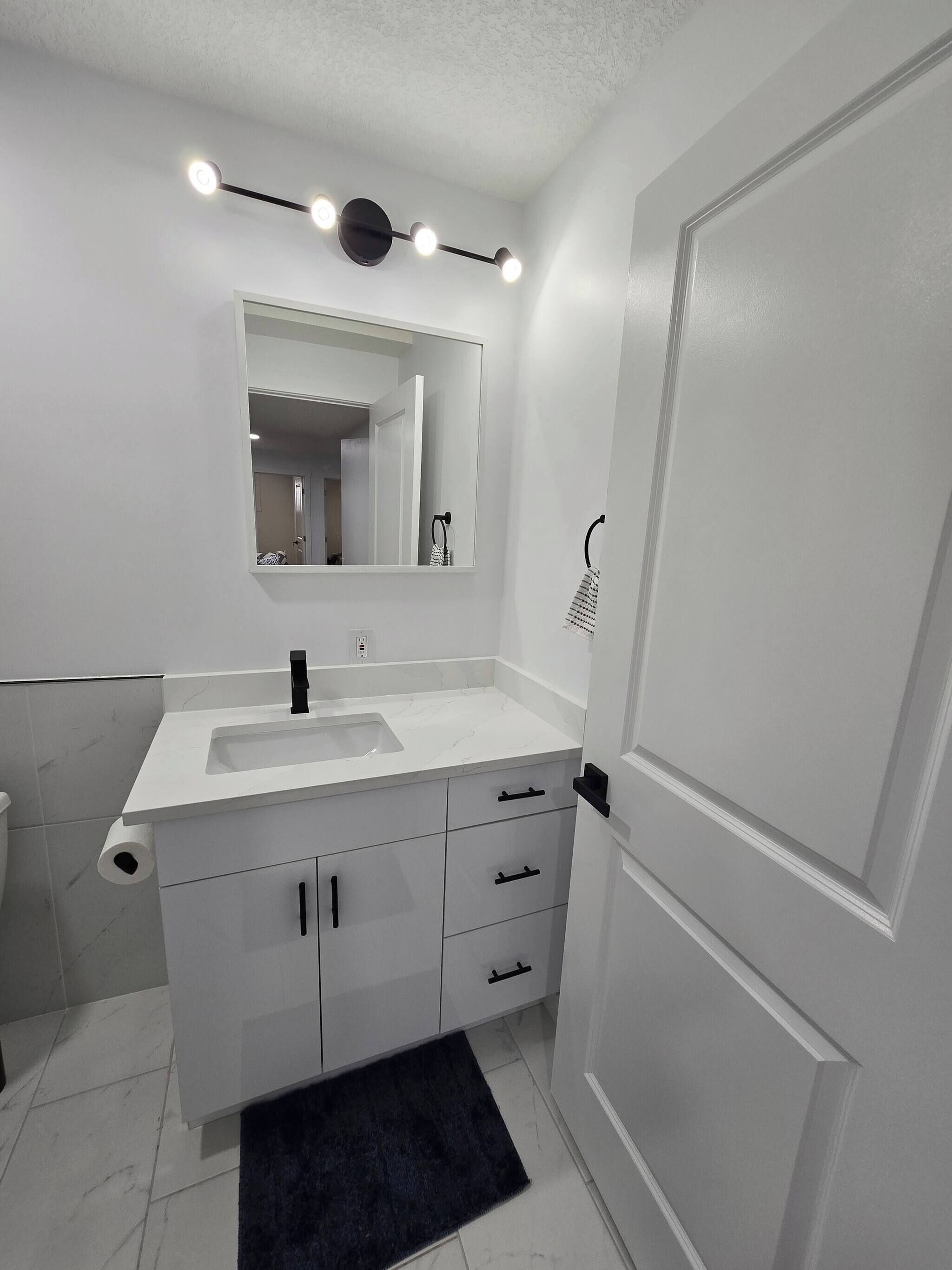 A modern bathroom with a white vanity, a large mirror, and a black towel rack.