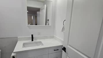 A modern bathroom with a white vanity, a large mirror, and a black towel rack.