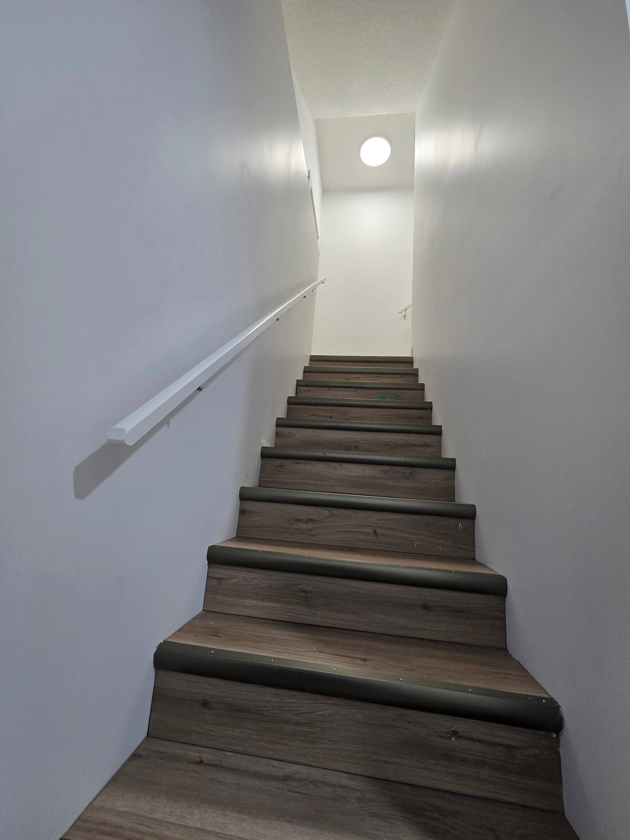 A staircase with wooden steps and white walls, leading to a landing with a ceiling light.