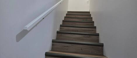 A staircase with wooden steps and white walls, leading to a landing with a ceiling light.