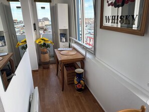 Ein Zimmer mit einem Holztisch, einer Vase mit Sonnenblumen, einer Dekorationsvase und einem Fenster mit Blick auf einen Hafen.