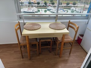 Een eettafel met twee gevlochten placemats, omringd door houten stoelen met beklede zitplaatsen, in een kamer met een groot raam dat uitkijkt op een jachthaven met boten.