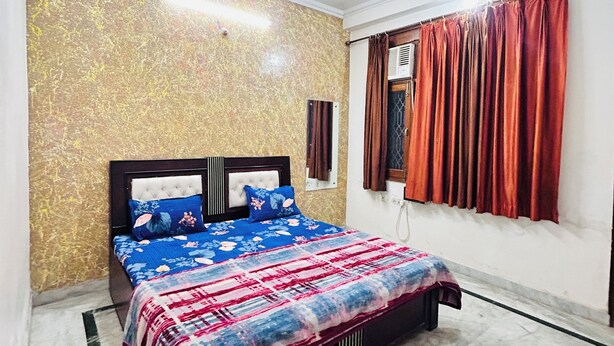 A bedroom with a bed, a ceiling fan, a window with curtains, and a wall with a textured pattern. - Superb 9-bedroom house with AC in charming Vrindavan (Vrindavan)