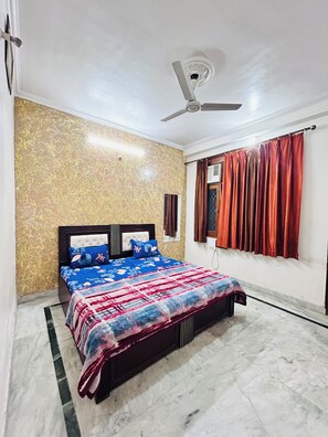 Une chambre à coucher comprenant un lit, un ventilateur de plafond, une fenêtre avec des rideaux et un mur orné d’un motif texturé.