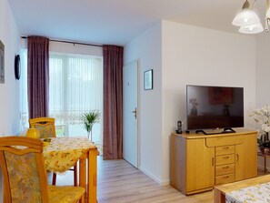 A room with a dining table, chairs, a TV, a cabinet, and a door leading to a balcony. - Apartment 'Ferienwohnung Mit 50qm' with Wi-Fi (Bad Soden-Salmünster)