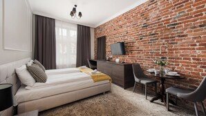 A modern hotel room with a brick wall, a bed with a yellow throw, a desk with a chair, and a flat-screen TV. - Sun & Snow Rakowicka Residence (Kraków)