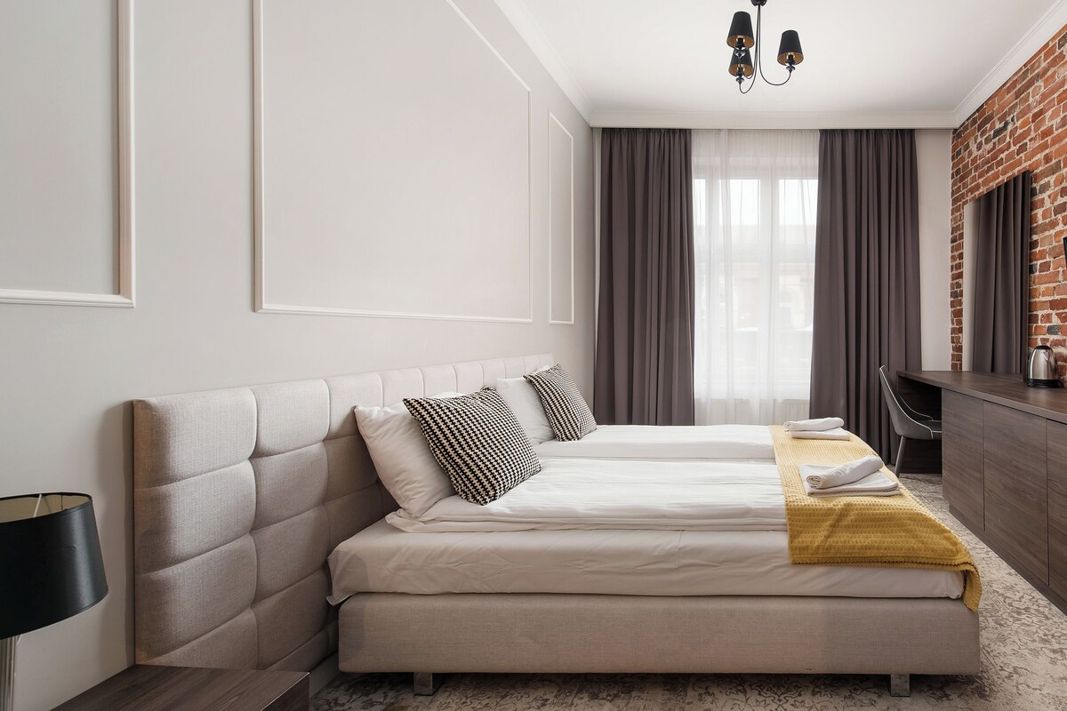 A modern hotel room with a bed, a desk, a television, and a brick wall.