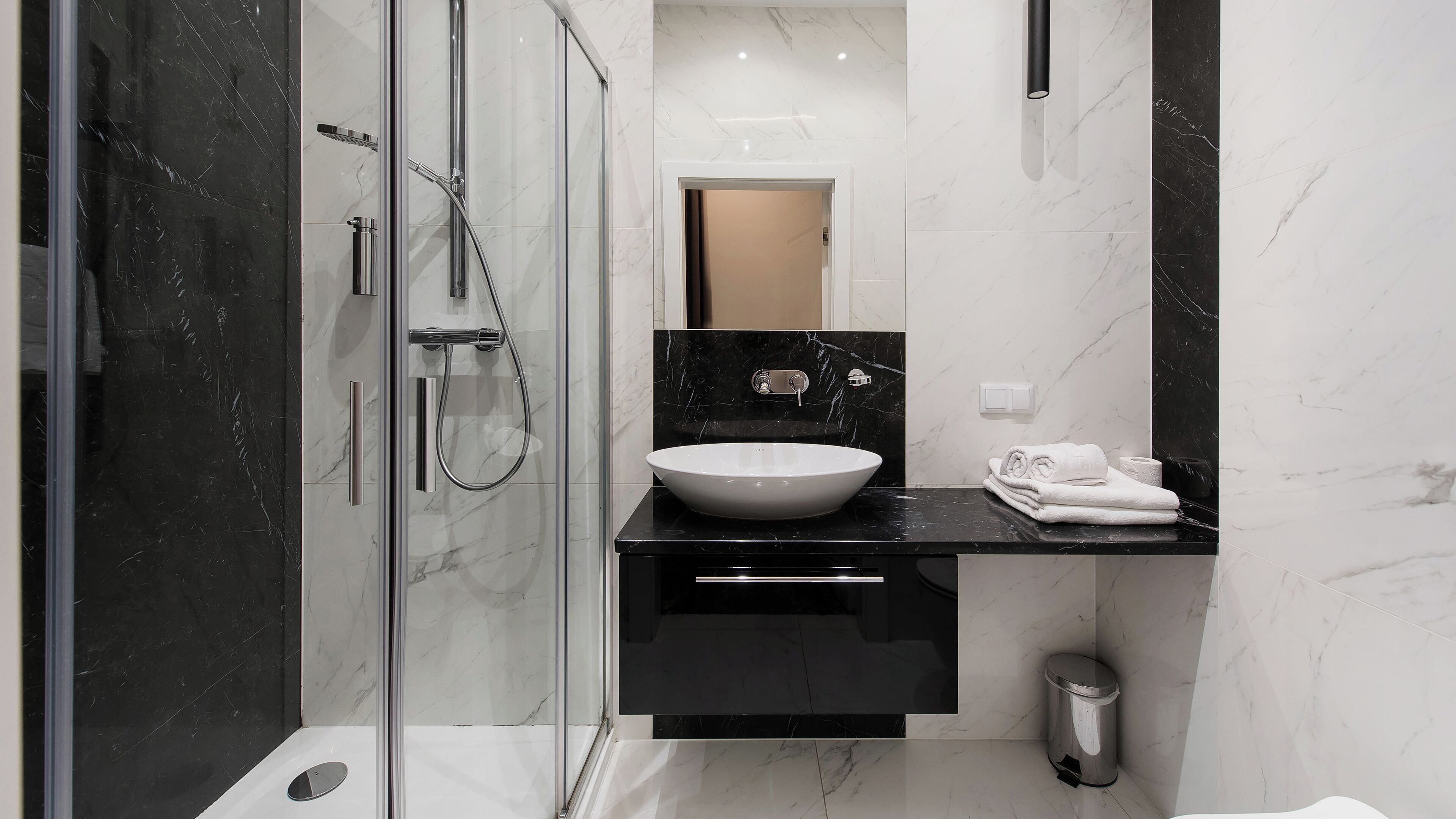 A modern bathroom with a glass-enclosed shower, a white sink, and a black countertop.