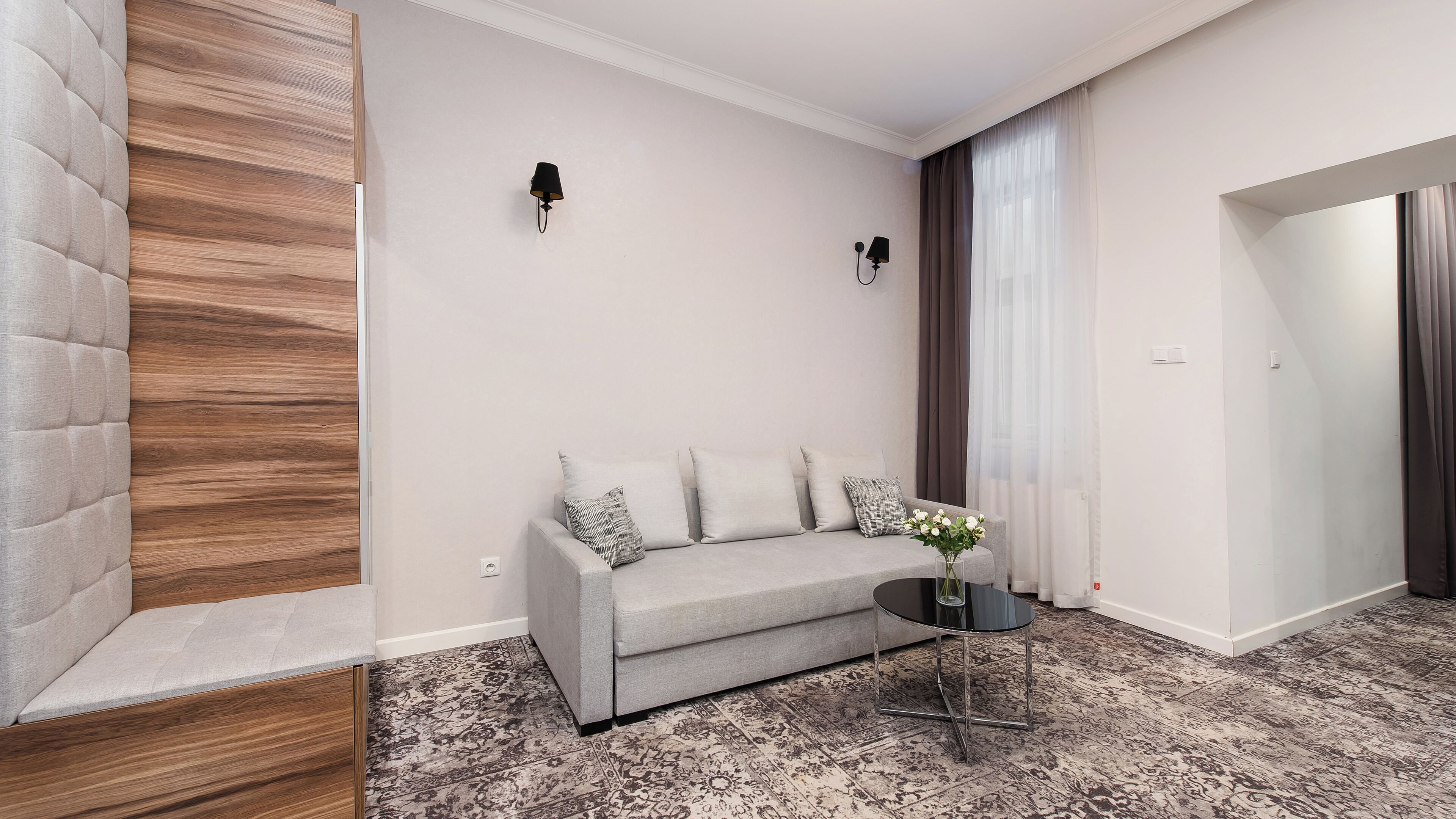 Una sala de estar moderna con un sofá gris, una mesita redonda con un jarrón y una alfombra estampada.