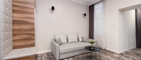 Una sala de estar moderna con un sofá gris, una mesita redonda con un jarrón y una alfombra estampada.