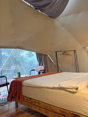 A tent with a bed, a chair, and a small table with a plant.