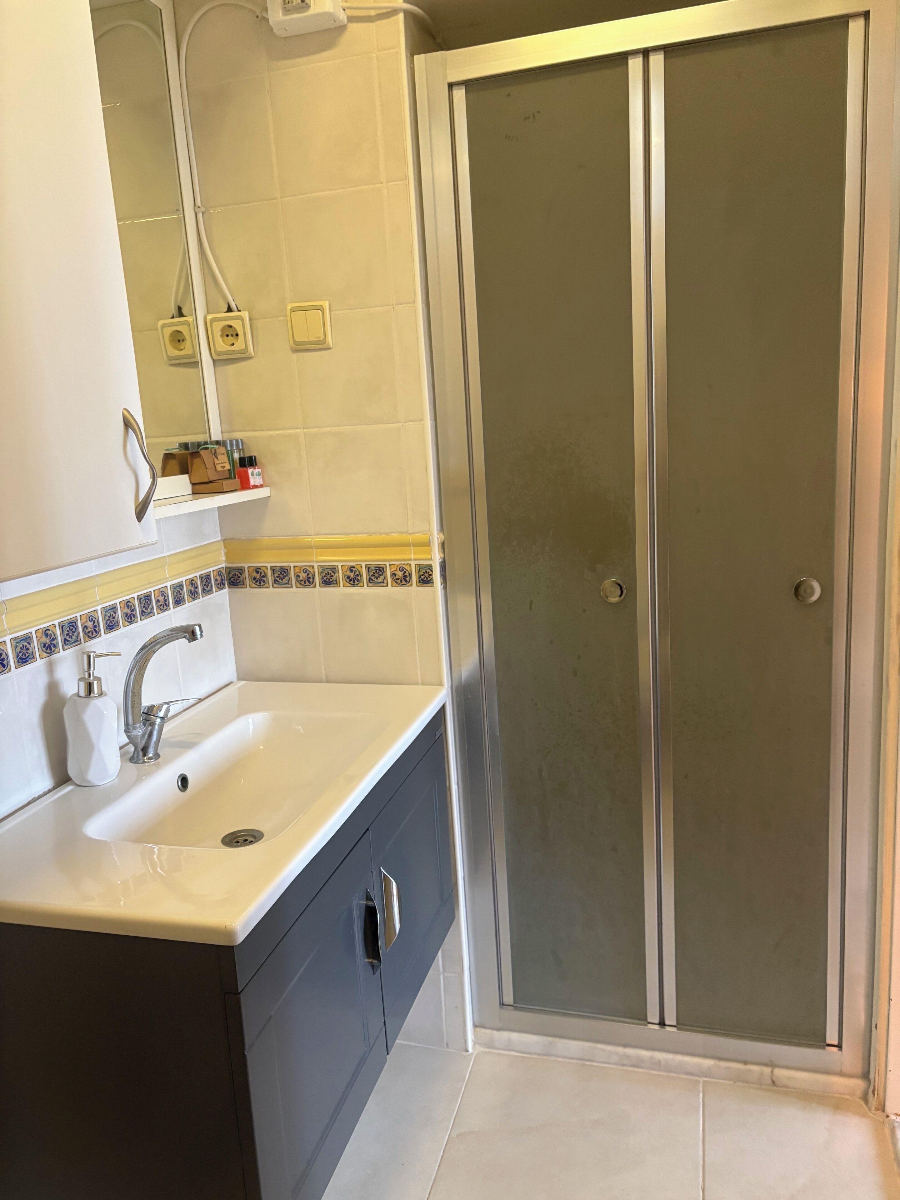 A bathroom with a white sink, dark cabinets, a mirror, and a glass shower enclosure.