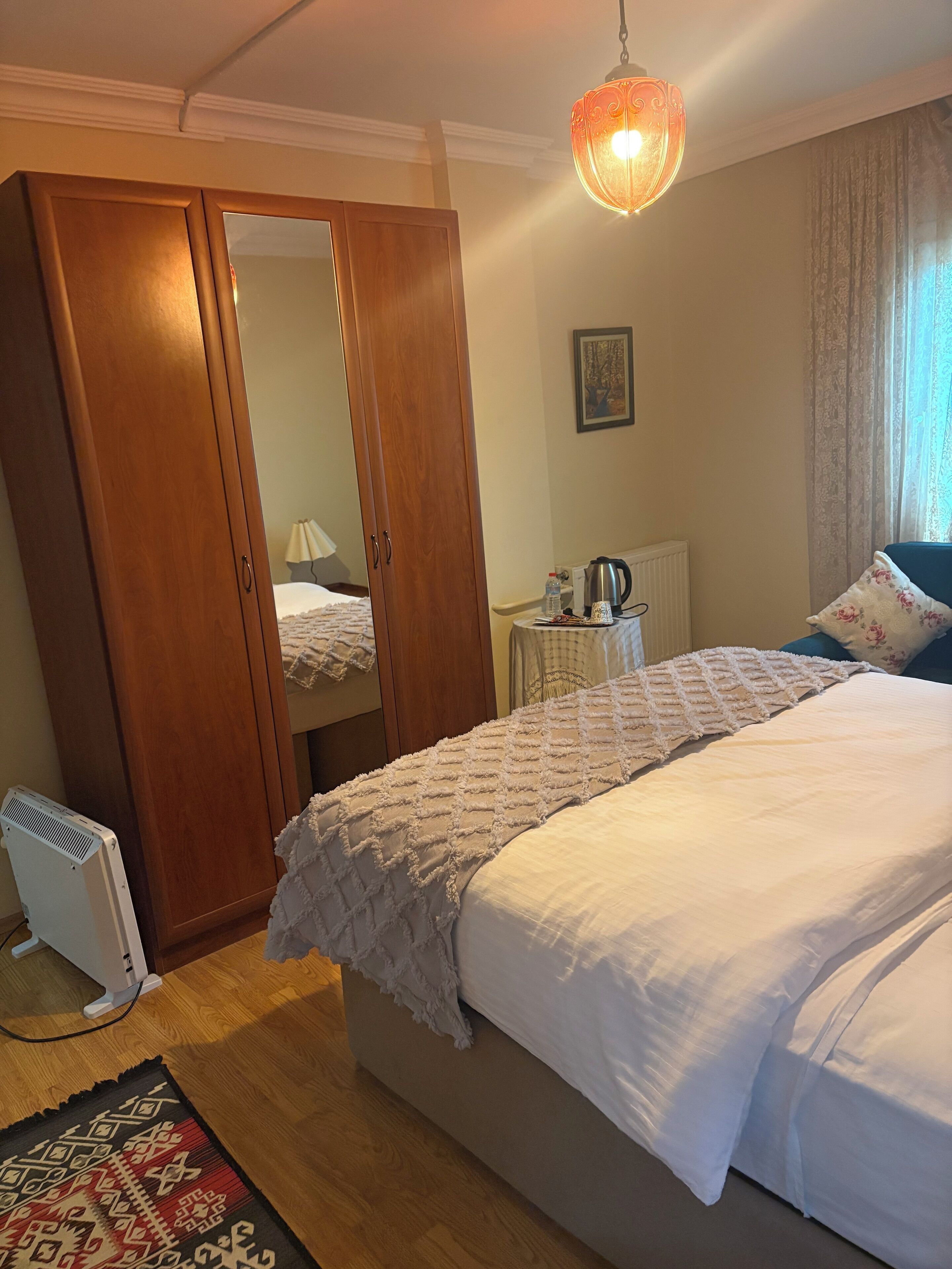 Een slaapkamer met een bed, een kledingkast, een radiator, een tafel met waterkoker en een hanglamp.