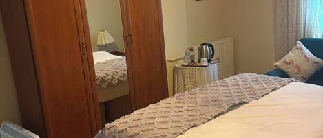 Een slaapkamer met een bed, een kledingkast, een radiator, een tafel met waterkoker en een hanglamp.