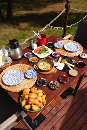 A wooden table set outdoors with various food items and a coffee maker.