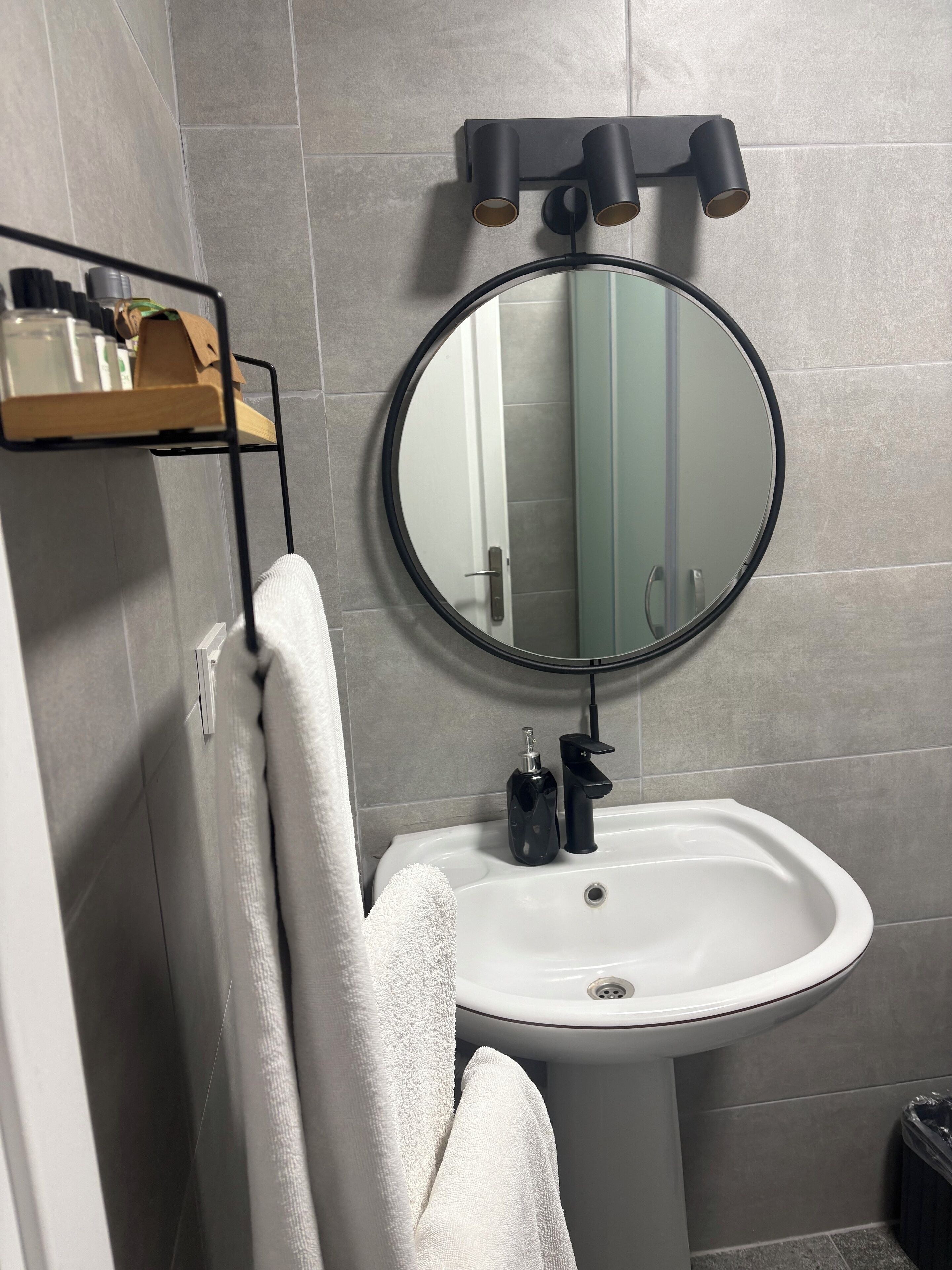 A bathroom with a round mirror, a white sink, and a towel rack.