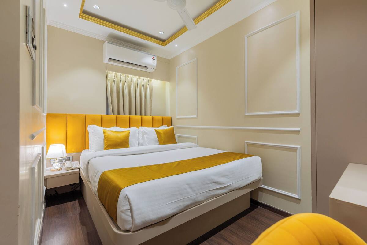 Ein Hotelzimmer mit Bett, Nachttisch, Lampe, Klimaanlage und Vorhängen.