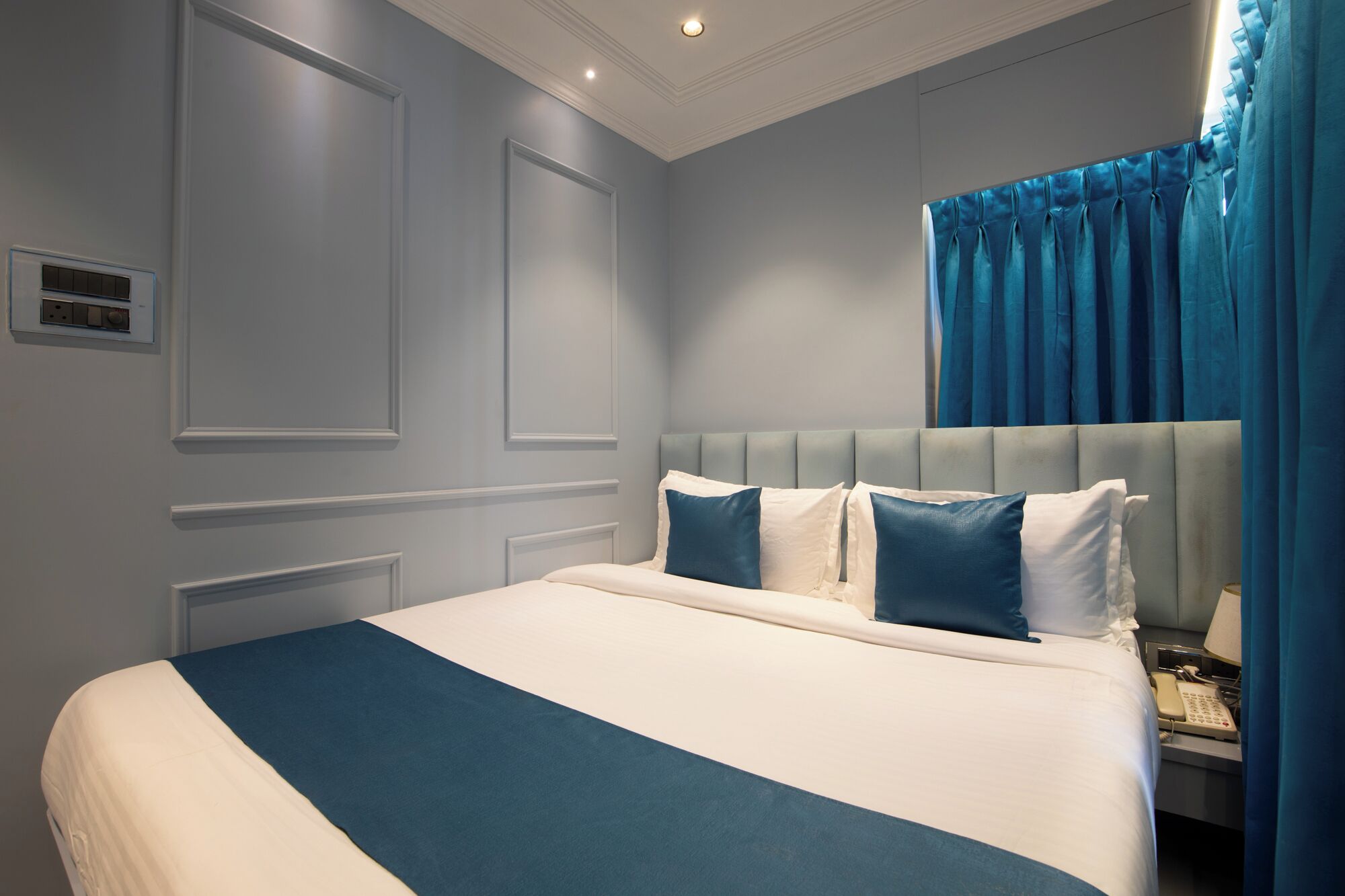 A neatly made bed with a blue and white bedspread, a tufted headboard, and a bedside telephone.