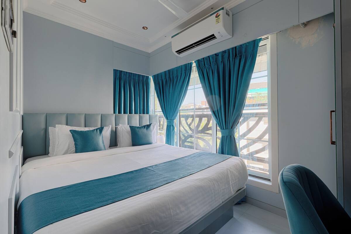 Ein modernes Hotelzimmer mit einem großen Bett, einer Kopfteil, einem Fenster mit Vorhängen und einer Klimaanlage.