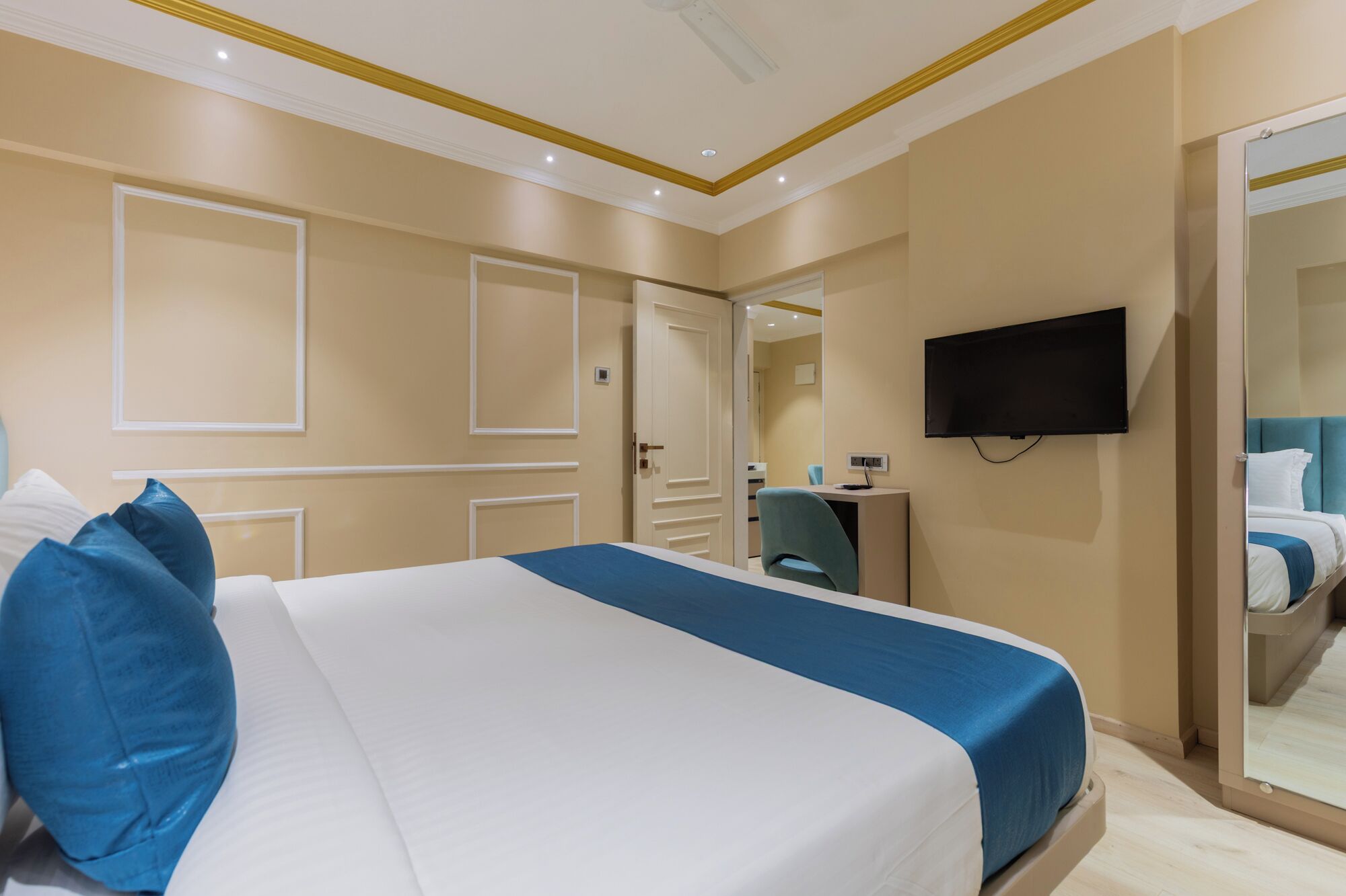 A hotel room with a large bed, a desk, a chair, a TV, and a mirror.