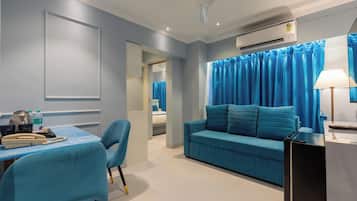 Habitación de hotel moderna con un sofá azul, un escritorio con teléfono y lámpara, y un equipo de aire acondicionado en la pared.