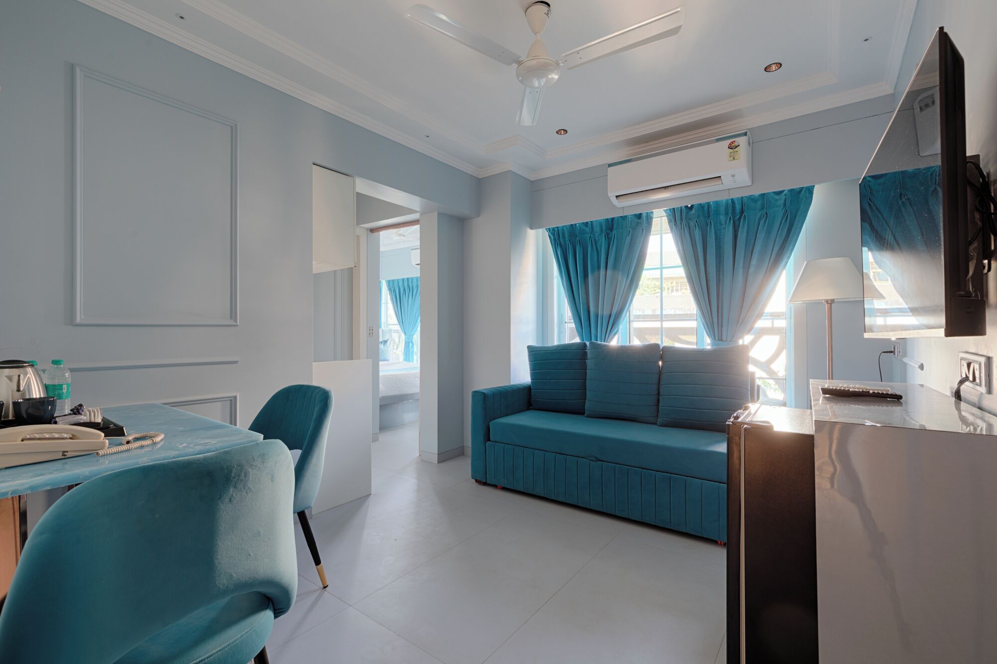Ein modernes Hotelzimmer mit einem blauen Sofa, einem Essbereich mit Tisch und Stühlen sowie einem an der Wand montierten Fernseher.