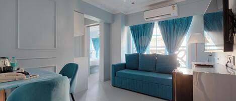 Ein modernes Hotelzimmer mit einem blauen Sofa, einem Essbereich mit Tisch und Stühlen sowie einem an der Wand montierten Fernseher.