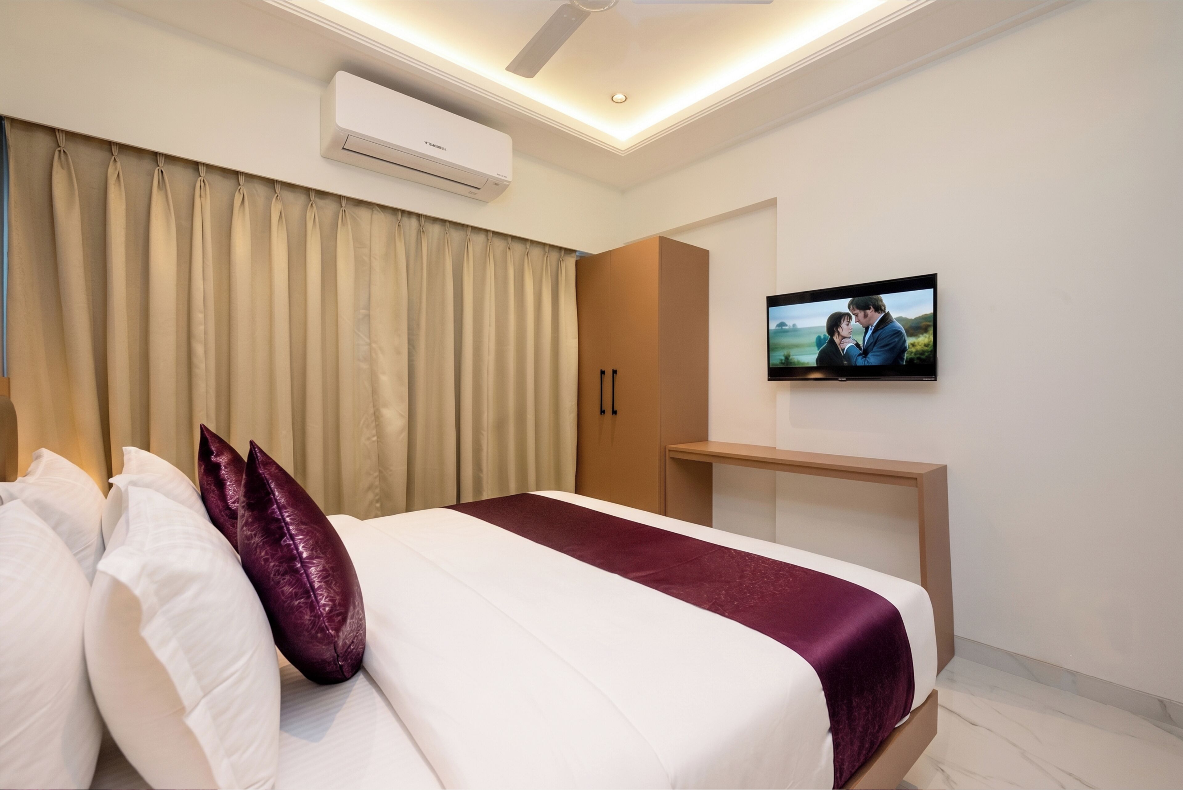 Une chambre d’hôtel moderne équipée d’un lit, de rideaux, d’un appareil de climatisation, d’une télévision et d’une armoire en bois.