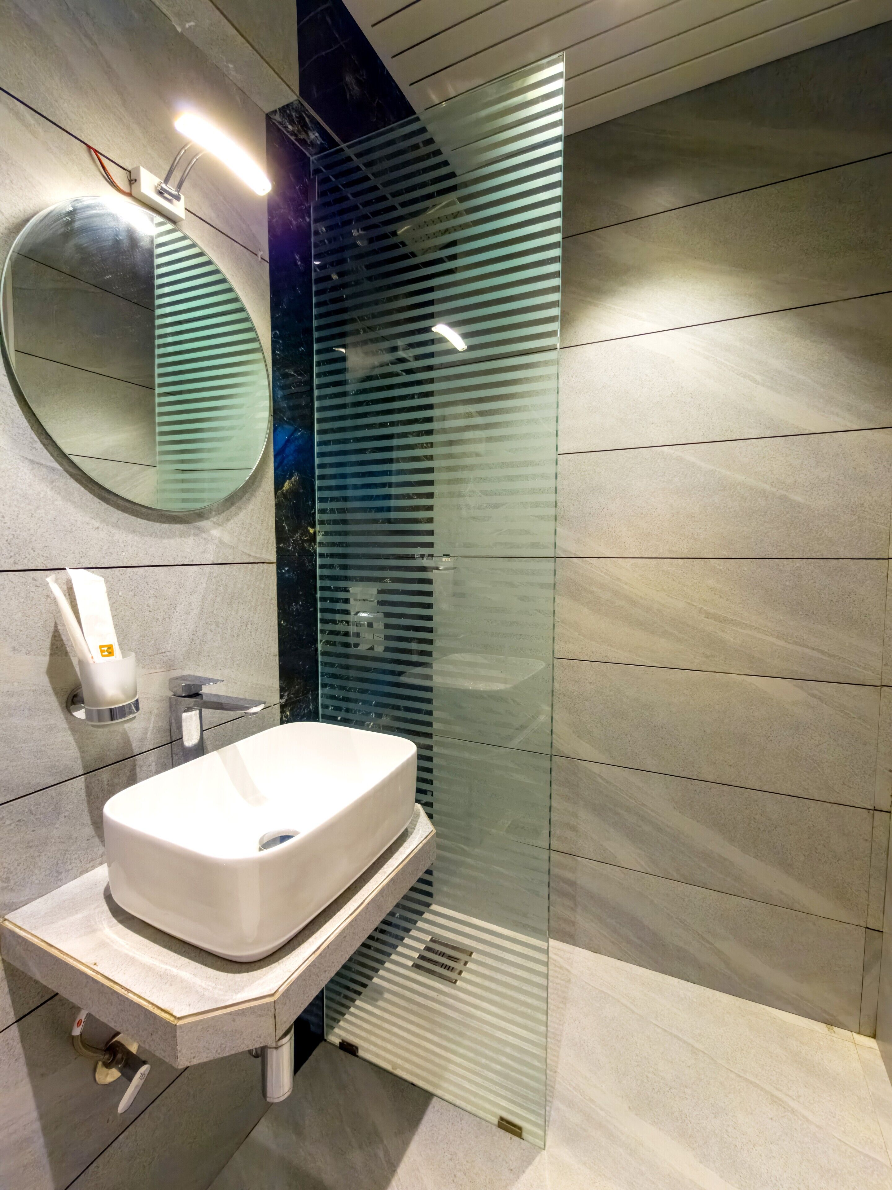 Un baño moderno con un lavamanos blanco, un espejo redondo y una cabina de ducha con paredes de vidrio.