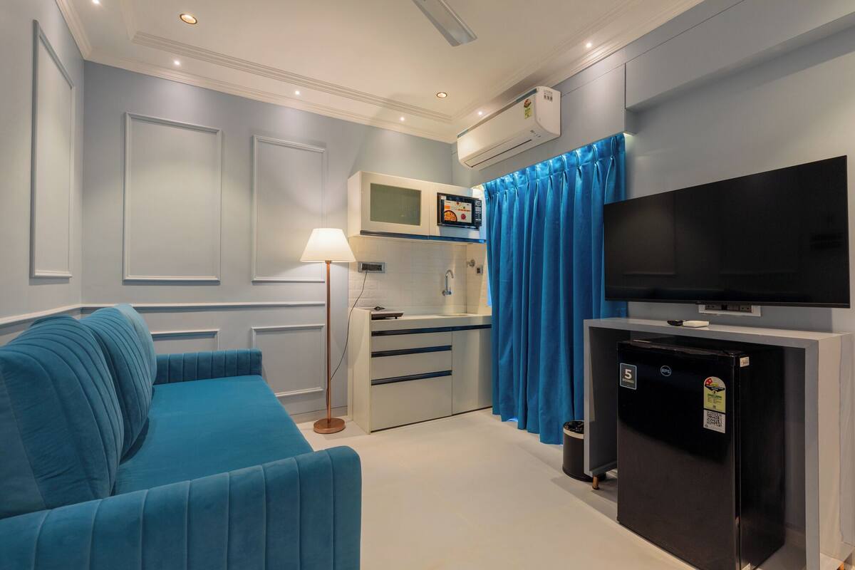Ein modernes Wohnzimmer mit einem blauen Sofa, einem Flachbildfernseher, einer Minikühlschrank und einer Küchenzeile mit einer Mikrowelle.