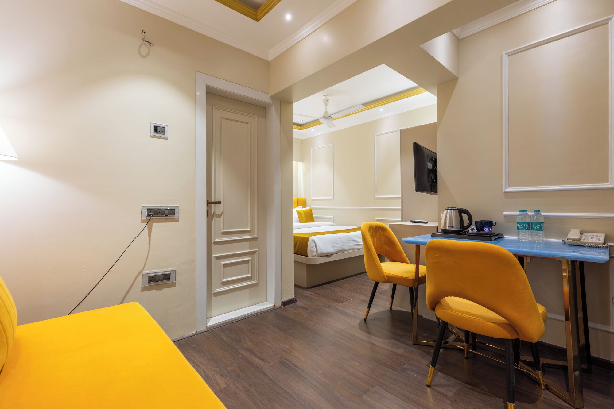 A hotel room with a bed, a desk with two chairs, a kettle, and a telephone.