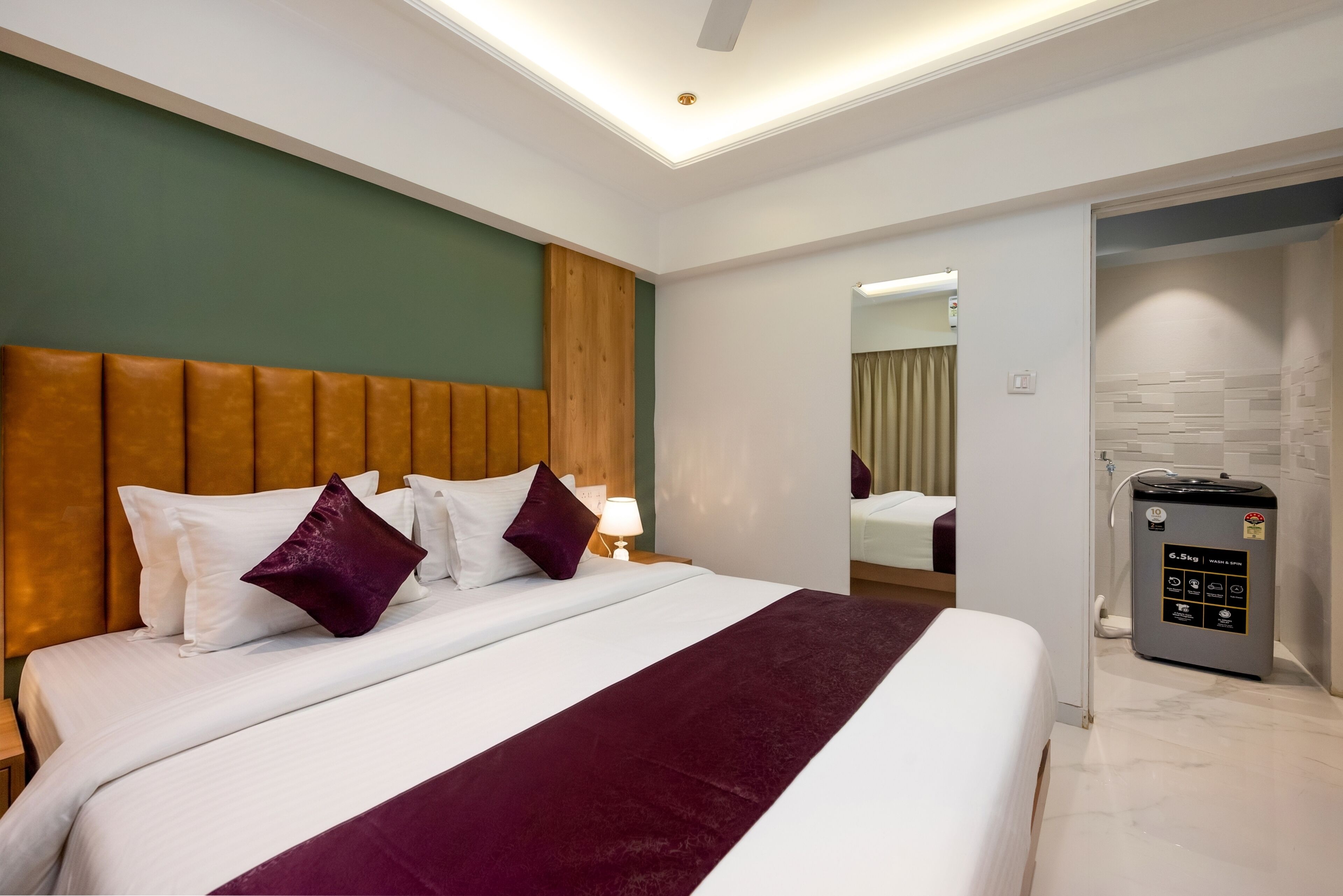 Habitación de hotel con una cama grande, cabecera de madera, un espejo, baño con ducha y minibar.