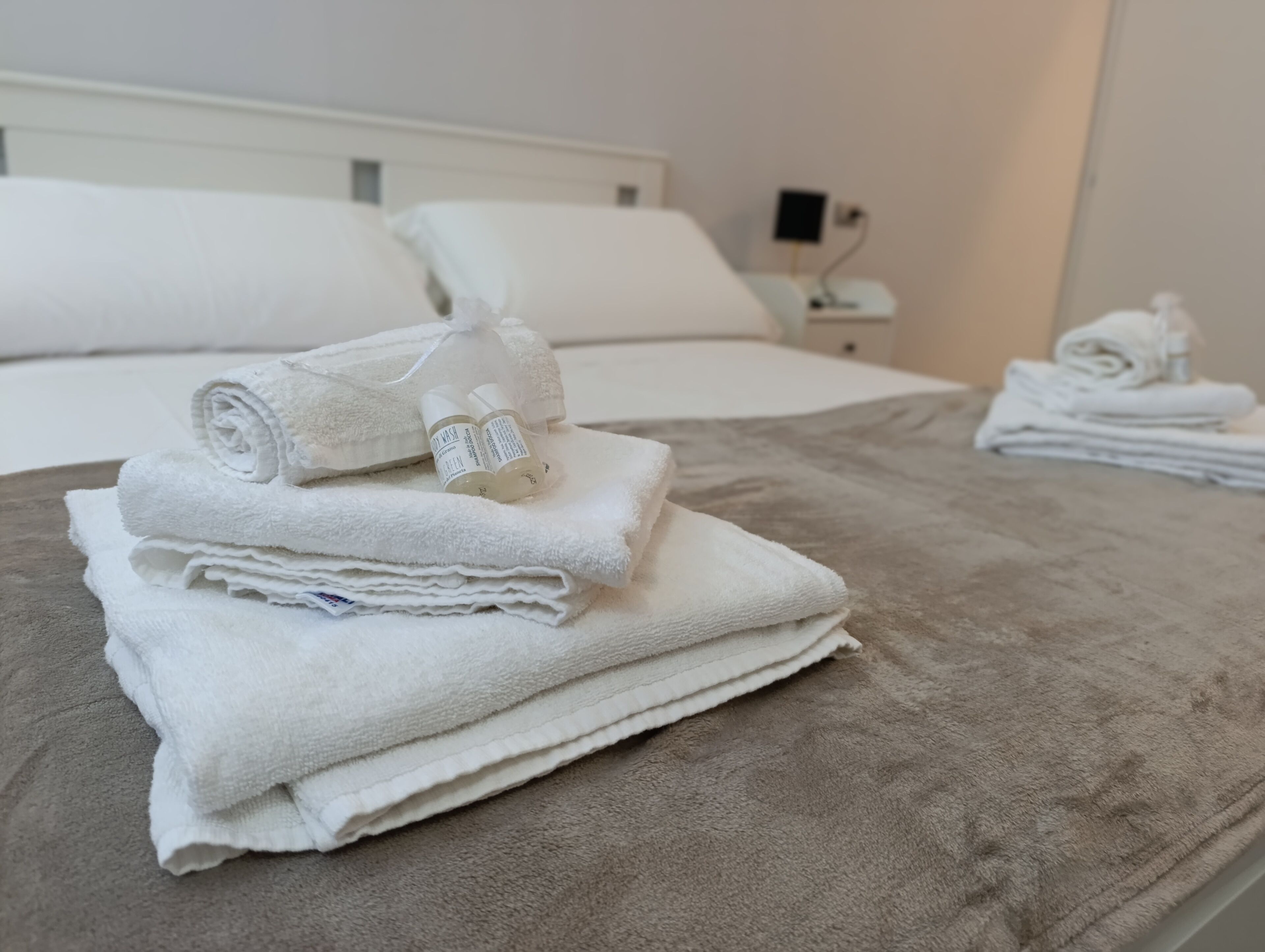 Un lit bien fait, avec des serviettes blanches et une bouteille de gel hydroalcoolique.
