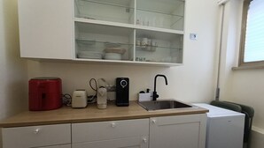 Ett kompakt kök med en arbetsbänk, ett handfat, ett kylskåp och ett glasskåp ovanför arbetsbänken.