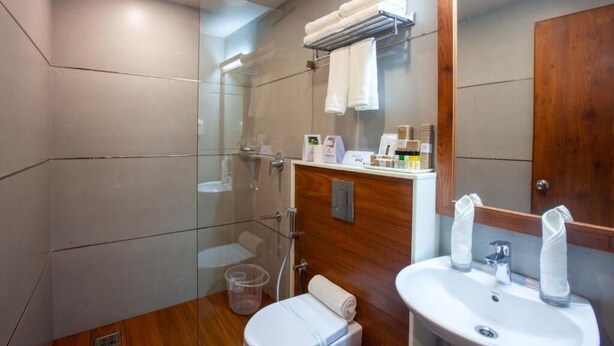 A modern bathroom with a glass shower enclosure, a wooden vanity, a sink, and a toilet. - Hotel Gentleman Plaza (Alappuzha)