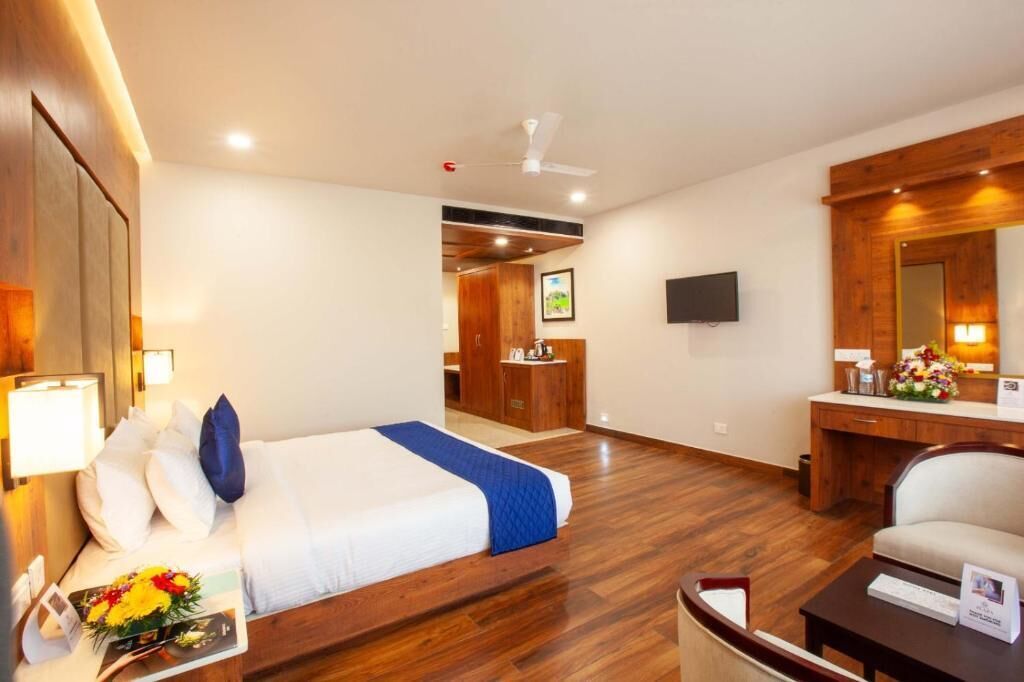 A hotel room with a bed, a desk, a chair, a TV, and a bathroom visible in the background.