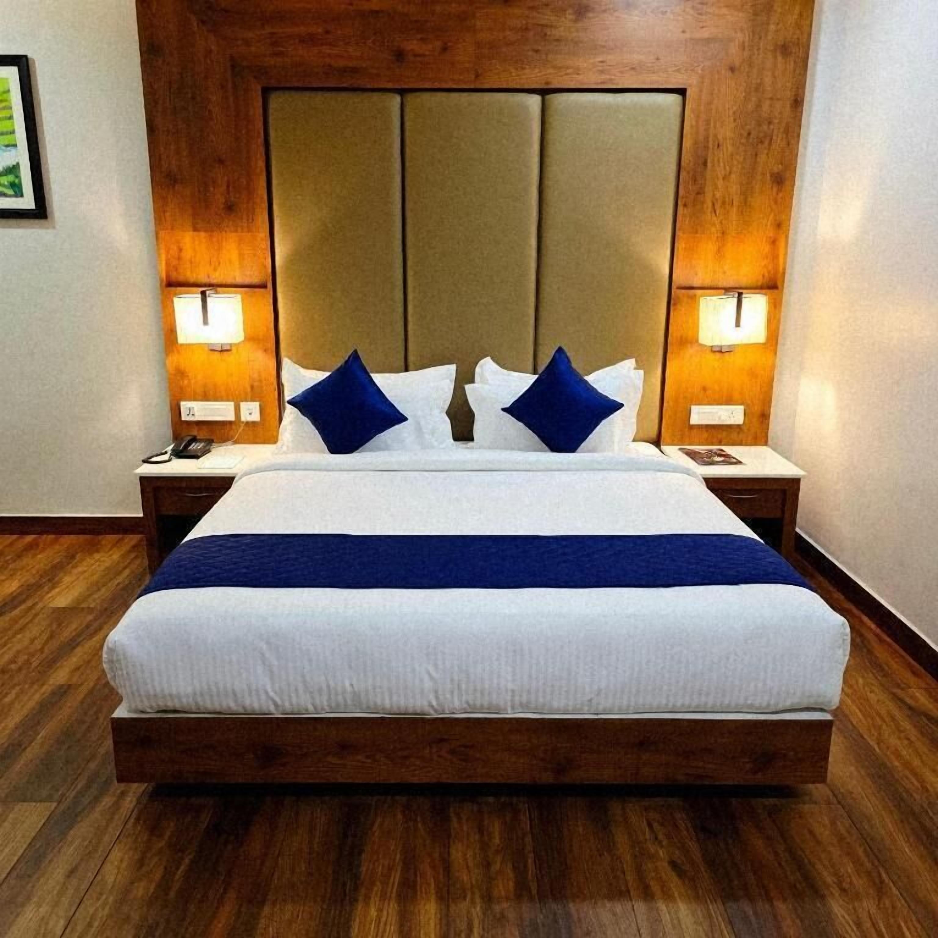 Una cama bien hecha con cabecera de madera, dos lámparas de noche y una almohada decorativa azul.