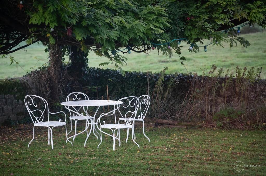 A white metal table and chairs set under a tree with a hedge in the background.