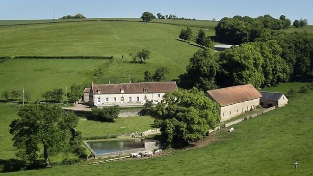A large, rectangular building with a flat roof, surrounded by lush green fields and trees. - domaine de Drémont (Anthien)