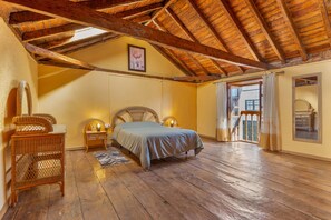 Ein Schlafzimmer mit Holzboden, einem Bett, einem Korbstuhl und einem Nachttisch mit Lampe.