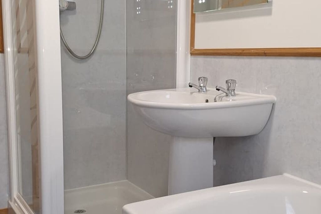 Une salle de bain avec un lavabo blanc, une douche et un miroir au-dessus du lavabo.